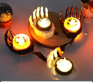 Close-up of glowing Halloween skeletal hand candle holders with pumpkin and web patterns.