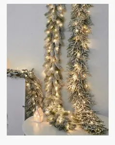 Detailed view of flocked Christmas garland featuring warm LED lights on a white table