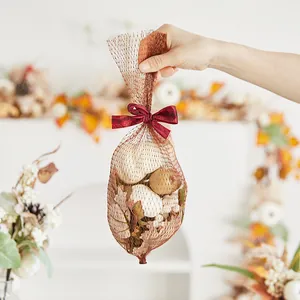 Autumn decorative mesh bag containing artificial white pumpkins and maple leaves