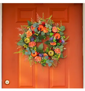 Artificial fall wreath with pumpkins and roses hanging on an orange door for Thanksgiving