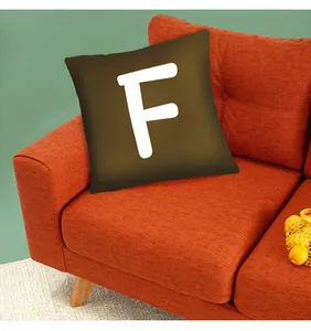 Detail view showing an olive green cushion cover featuring a bold white letter F on a sofa