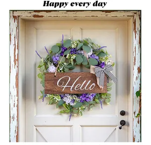 Dettaglio ghirlanda di eucalipto con fiori viola e insegna Hello in legno su porta bianca.