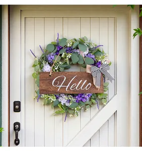 Dettaglio di una ghirlanda di eucalipto con targa 'Hello' su una porta di legno bianca.
