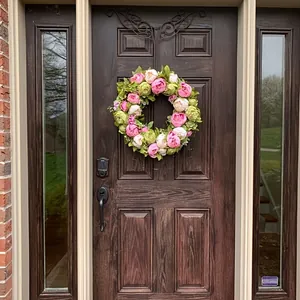 Ghirlanda di peonie artificiali primaverili appesa a una porta d'ingresso in legno scuro