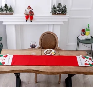 Festive red Christmas table runner with embroidered gnome details on a wooden table.