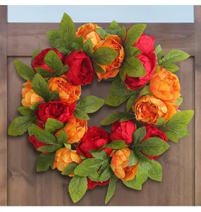 Detailed view of artificial red and yellow peony wreath with lush green leaves