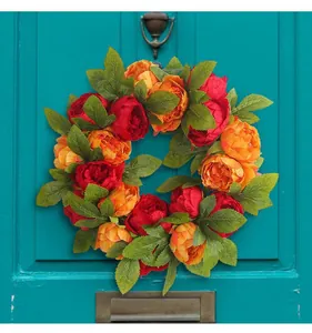 Detailed view of vibrant red and orange peony wreath hanging on a stylish teal door decoration.