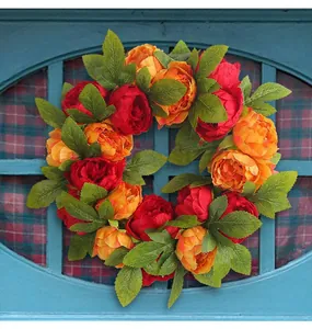 Vibrant red and orange artificial peony wreath hanging on a blue wooden window