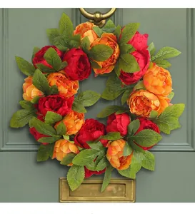 Close-up detail of a red and orange artificial peony wreath hanging on a green door