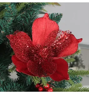 Close-up of a festive red glitter magnolia flower on a green Christmas tree branch.