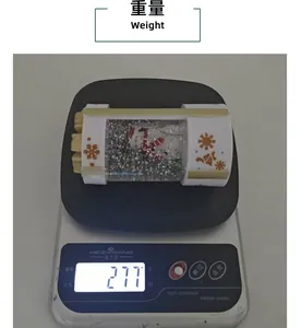 Macro shot of a Christmas snow globe lantern being weighed on a scale, showing 277g.