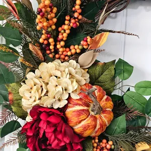 Close-up of autumn wreath featuring a rustic pumpkin, red hydrangea, and berries for decor.
