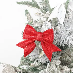 Red glittery Christmas bow ornament hanging on a snowy frosted pine tree branch
