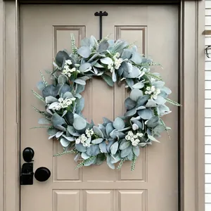 Corona decorativa de oreja de cordero con flores blancas colgada en puerta marrón.