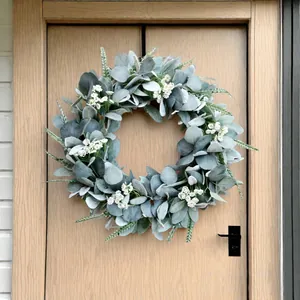 Corona de hojas de oreja de cordero verde plateado con flores blancas en una puerta de madera clara.