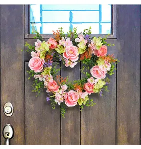 Heart-shaped pink rose wreath with lush greenery hanging on a dark wood door for decor