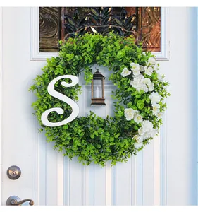 Detail van een eucalyptuskrans met witte letter S en kleine lantaarn op witte deur