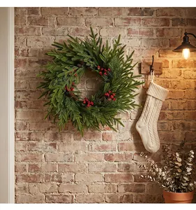 Detailed view of a lush Christmas wreath with red berries on a rustic brick wall