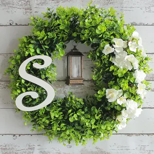 Kunstmatige eucalyptuskrans met witte letter S en lantaarn voor kerstversiering aan de deur