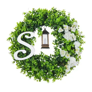Kunstmatige eucalyptuskrans met witte bloemen, letter S en decoratieve lantaarnlamp.