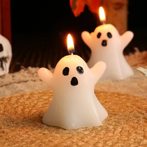 Two cute white ghost-shaped Halloween candles lit on a rustic woven mat for atmosphere