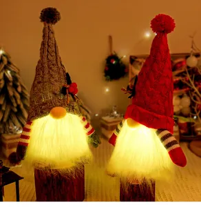 Two glowing Christmas gnomes with knitted grey and red hats on rustic wooden logs