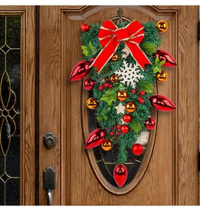 Festive Christmas teardrop wreath with red bow and ornaments hanging on a wooden door.