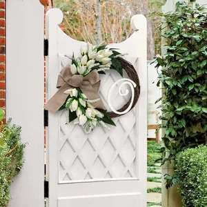 Gedetailleerd zicht op witte tulpenkrans met alfabetletter op een tuinpoort
