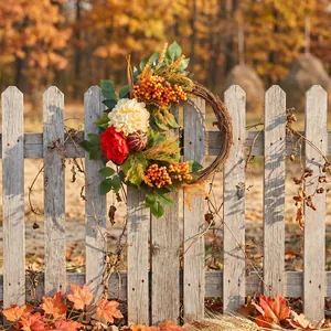 Autumn harvest wreath with red flowers and pumpkin on a rustic wooden picket fence