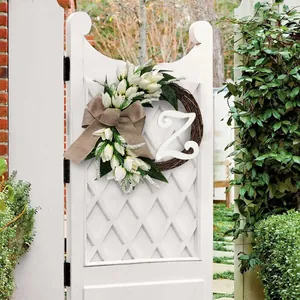 Detail van een witte tulpenkrans met jute strik en de letter Z hangend aan een tuinhek