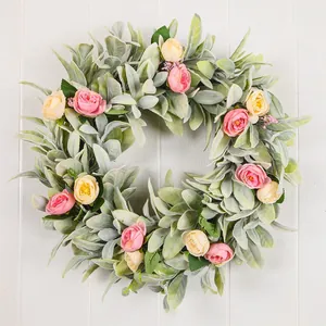 Detail shot of a lush lamb's ear wreath with pink and yellow roses on white wood.