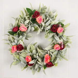 Close-up detail of decorative lamb's ear wreath with pink and red roses on white wall