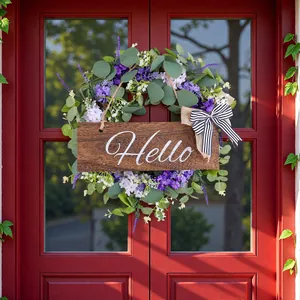 Corona di eucalipto artificiale con fiori viola e scritta Hello su una porta rossa.