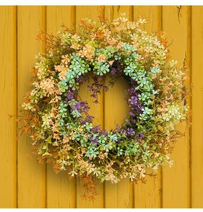 Colorful wildflower wreath detail with vibrant plastic flowers on yellow wooden background.