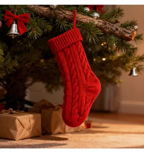 Close-up of red cable knit Christmas stocking hanging on tree with gift boxes background