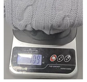 Detail view of a grey cable-knit Christmas stocking on a digital scale showing 109g