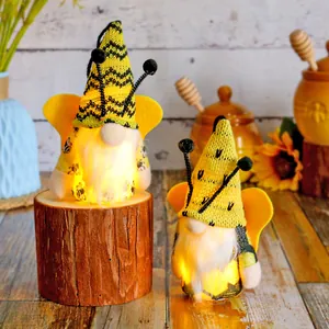 Two glowing bee festival gnomes with warm LED lights and yellow wings on rustic wood stump