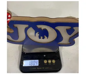 Close-up of a blue Christmas wooden JOY hanging ornament weighing 180.4 grams on a scale