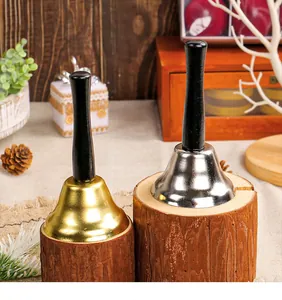 Close-up detail of gold and silver Christmas handbells with black wooden handles on rustic logs