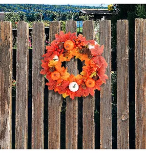 Detail van een herfstkrans met witte pompoenen en esdoornbladeren aan een houten hek