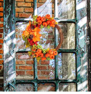 Detailed view of harvest wreath with pumpkins and maple leaves on a rustic window frame