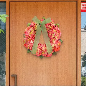 Dettaglio ghirlanda di ortensie finte con nastro verde appesa a una porta in legno
