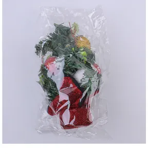 Detailed view of mini Christmas tree ornament with pine needles and red berries in plastic bag.