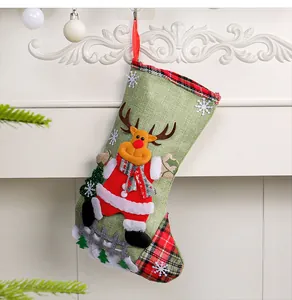 Detail of a linen Christmas stocking with a 3D reindeer and red plaid accents hanging on a mantel