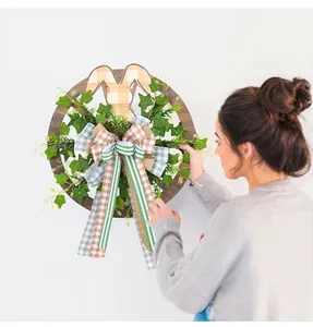 Femme accrochant une couronne de Pâques en bois avec lapin et lierre sur un mur.