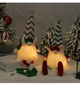 Close-up of glowing Christmas gnomes with knitted hats and warm LED lights in snow