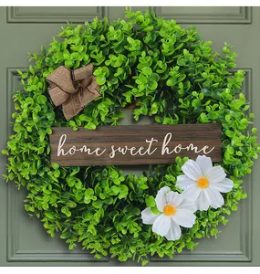 Close-up of green leaf wreath with white flowers and 'home sweet home' sign on door