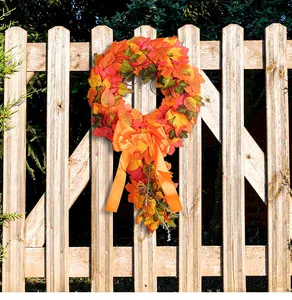 Decorative autumn harvest wreath with orange maple leaves and a large bow on a fence