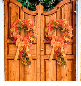 Decorative pair of autumn maple leaf wreaths with orange bows hanging on a rustic wooden door.