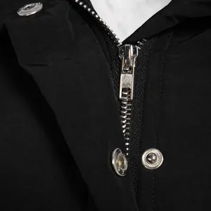 Close-up detail of smooth metal zipper and snap buttons on black winter parka